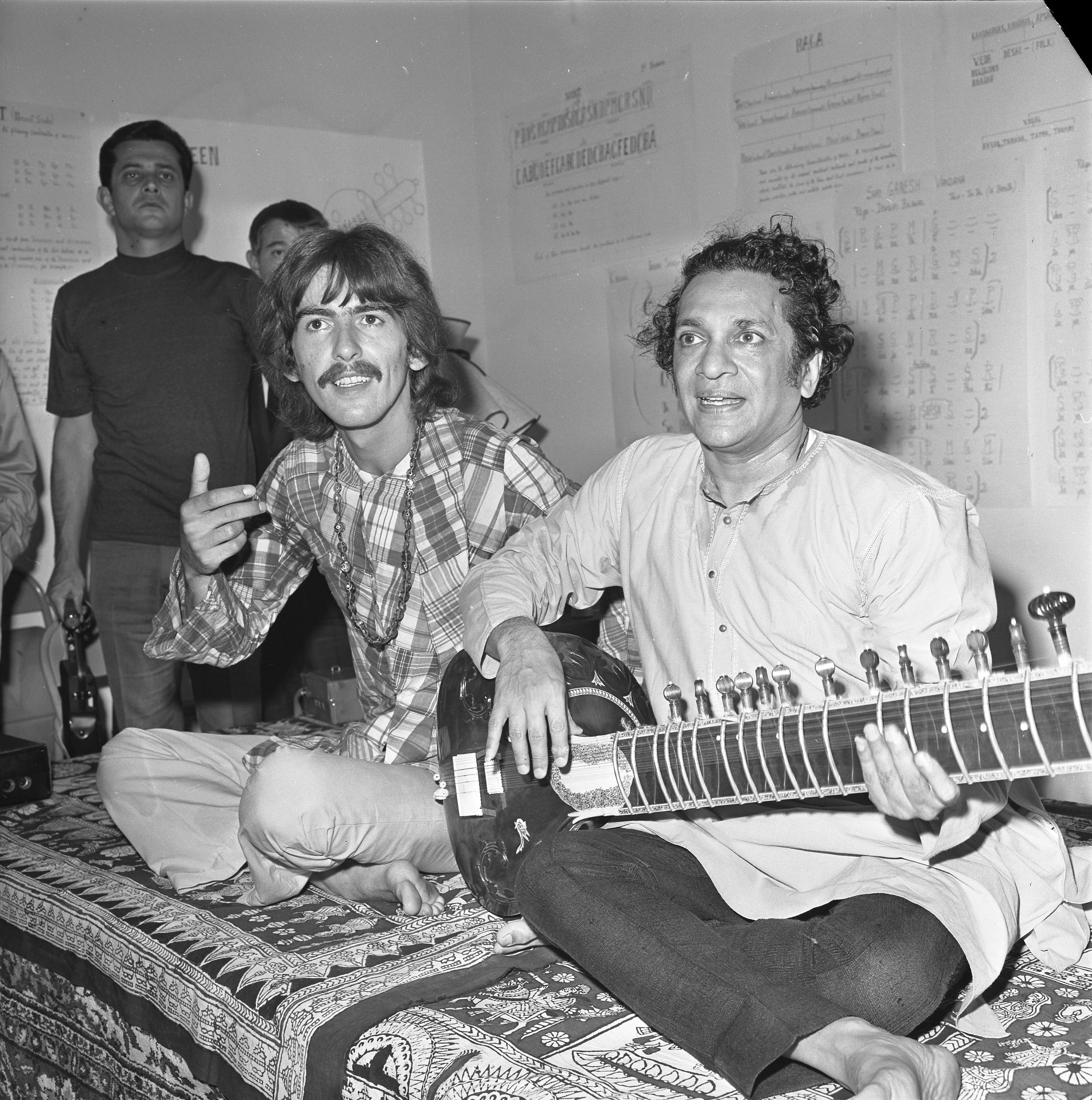 George Harrison sitting by Ravi Shankar, who is playing the sitar